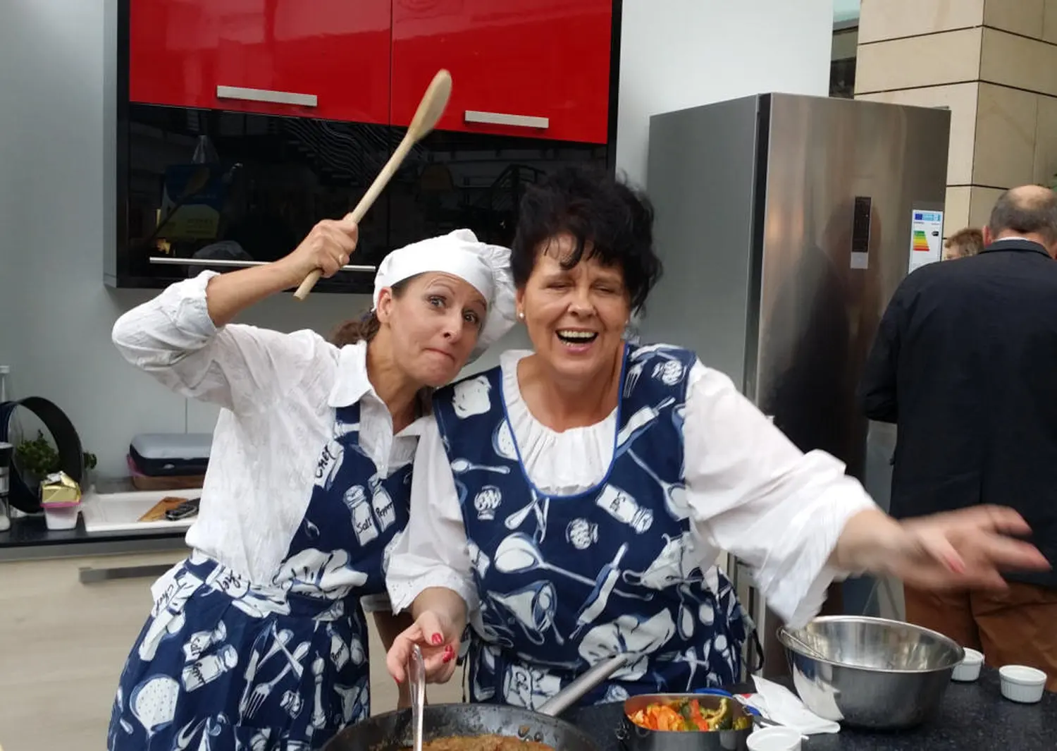Moments Veranstaltungsagentur - Zwei Frauen in Schürzen kochen lachend